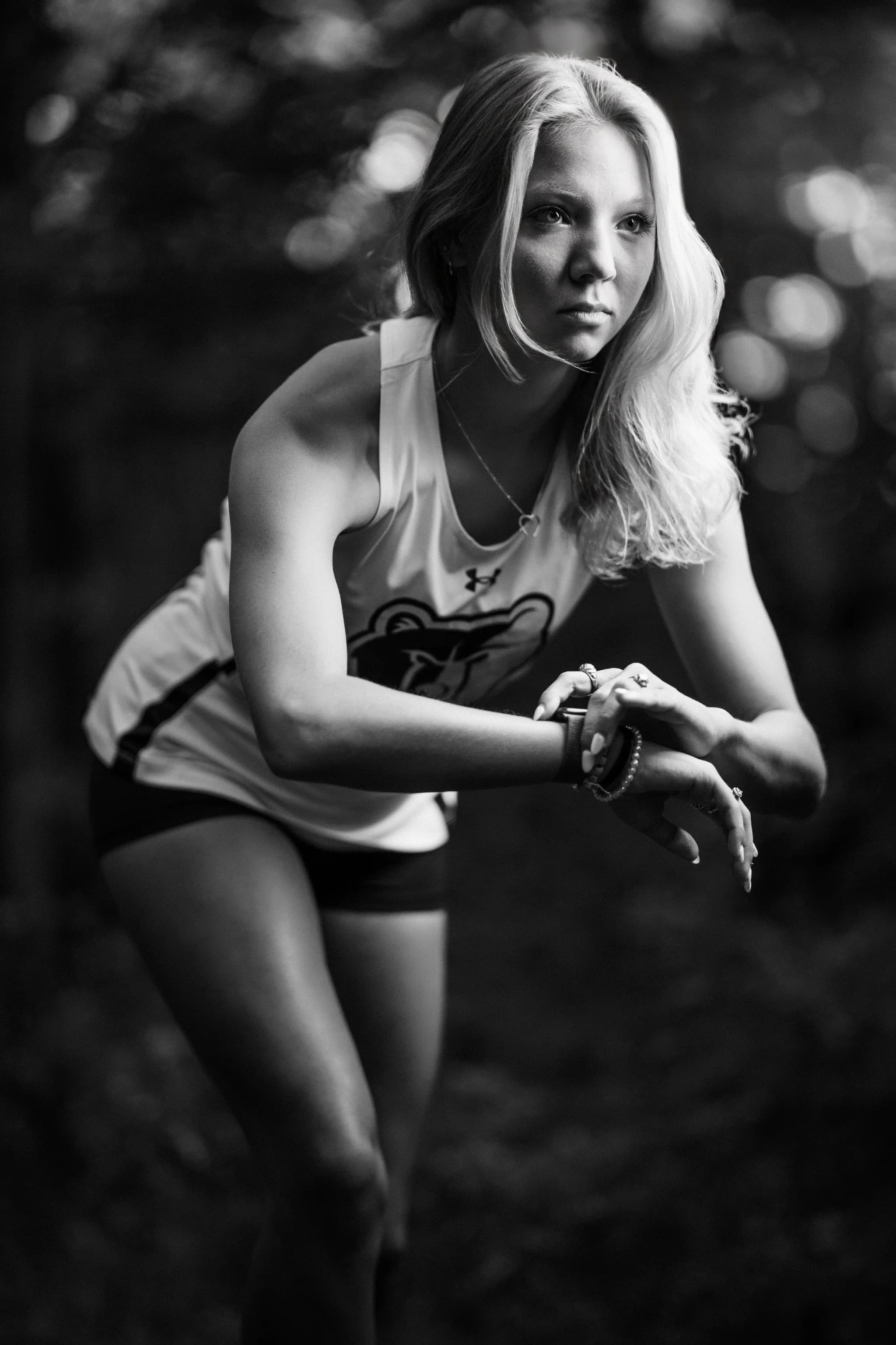 Black-and-white portrait of a senior athlete in her track uniform checking her watch mid-stretch