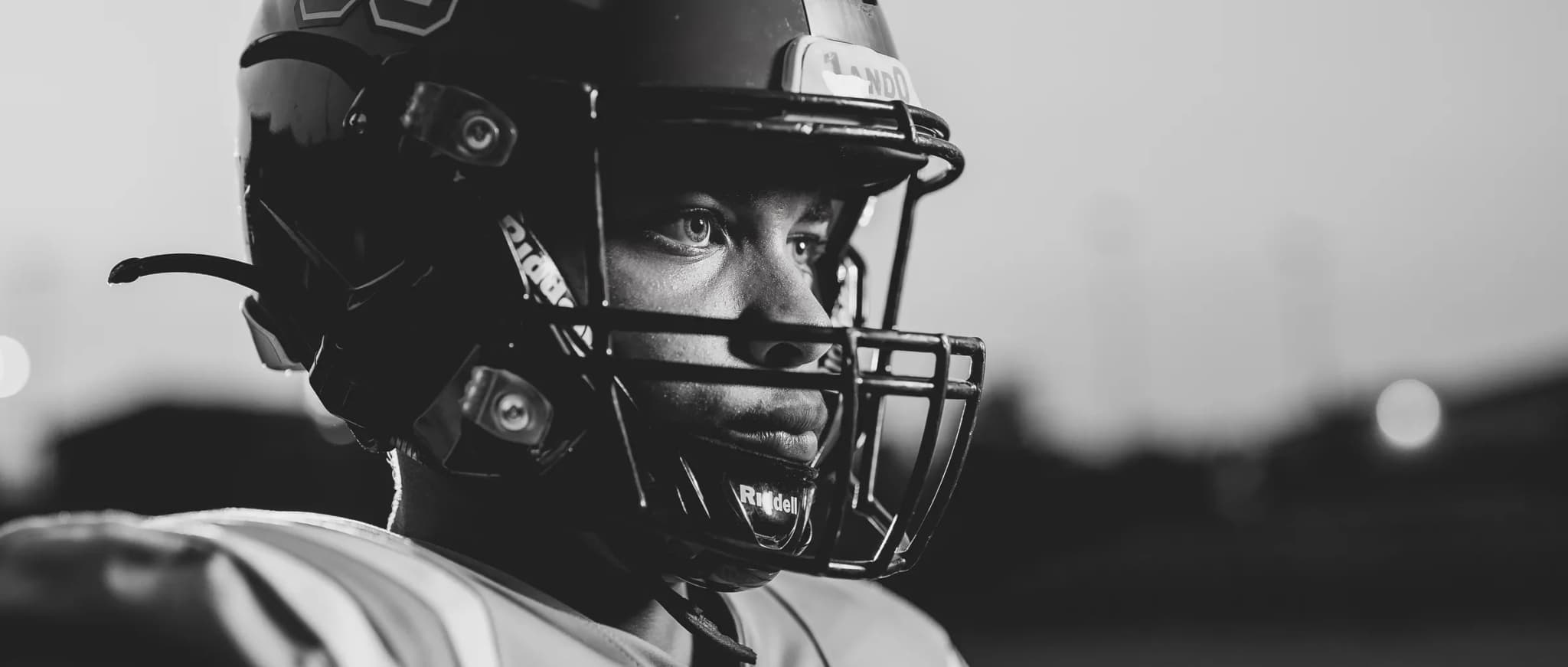 Dramatic black-and-white close-up of a senior football player in his helmet under the lights