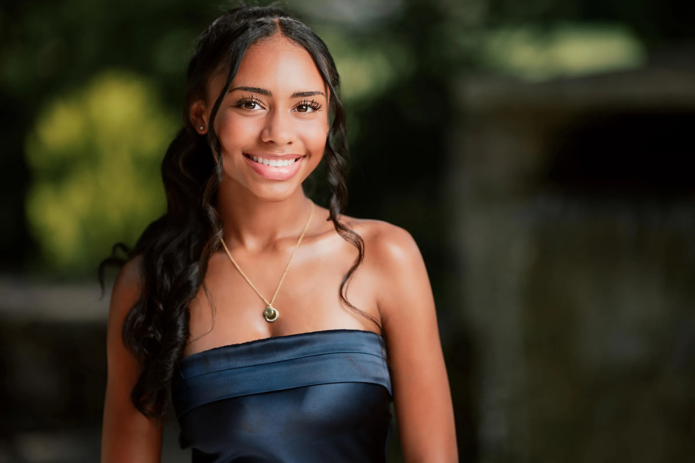 Warm portrait of a smiling girl in a navy satin dress with a gold pendant necklace