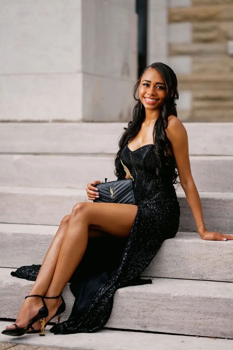 Prom portrait in a sequined black gown seated on grand stone steps at golden hour