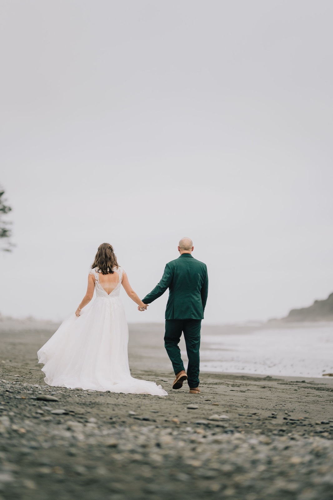 Newlyweds walking toward the sea stacks along the foggy shoreline of Rialto Beach