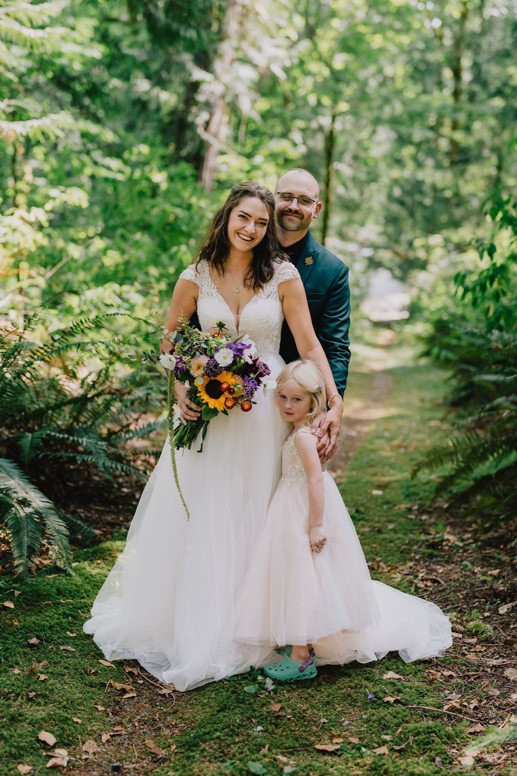 Bride holding a wildflower bouquet beside her daughter in the rainforest