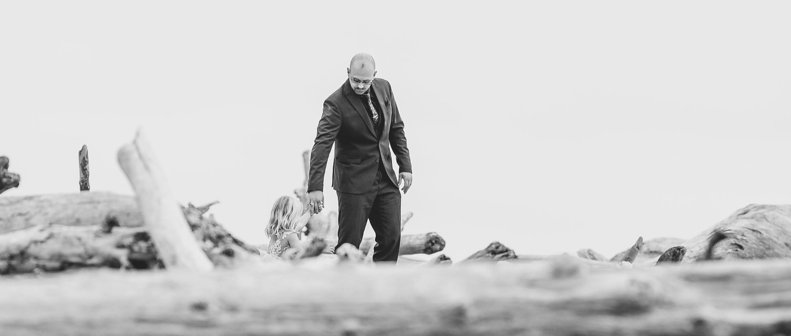 Adriana and Mitchell standing tiny among giant driftwood and sea stacks at Rialto Beach, black and white panorama