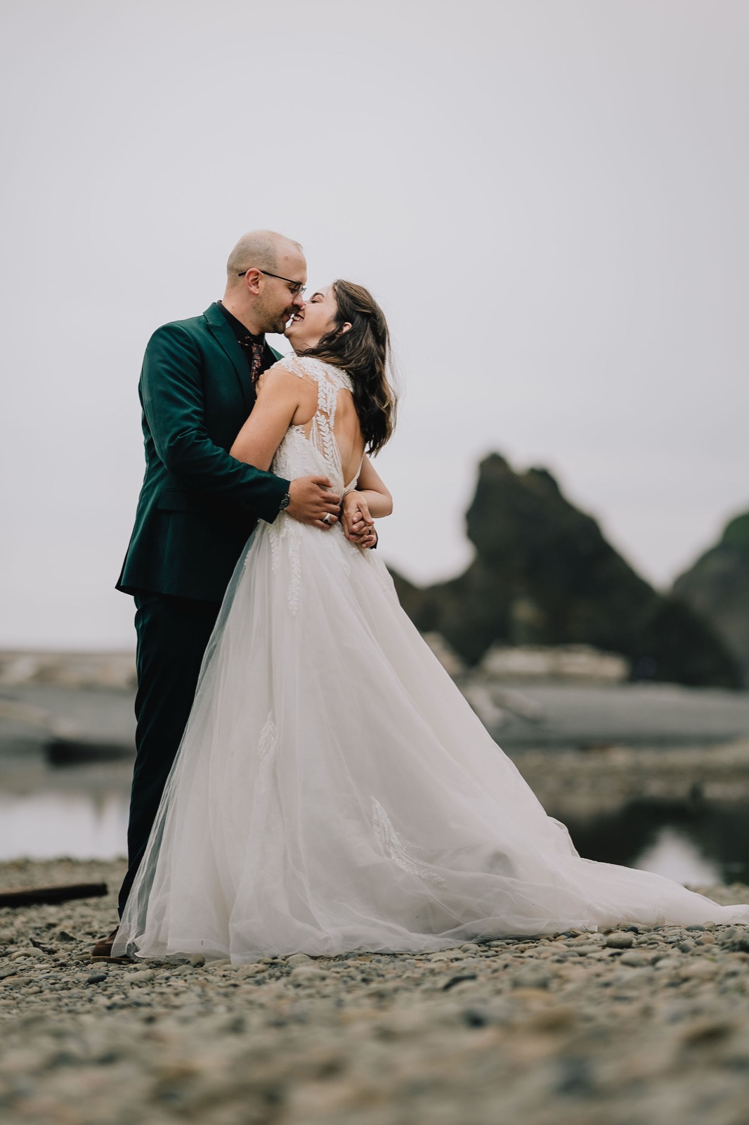 Couple kissing in the fog with sea stacks behind them on the Washington coast