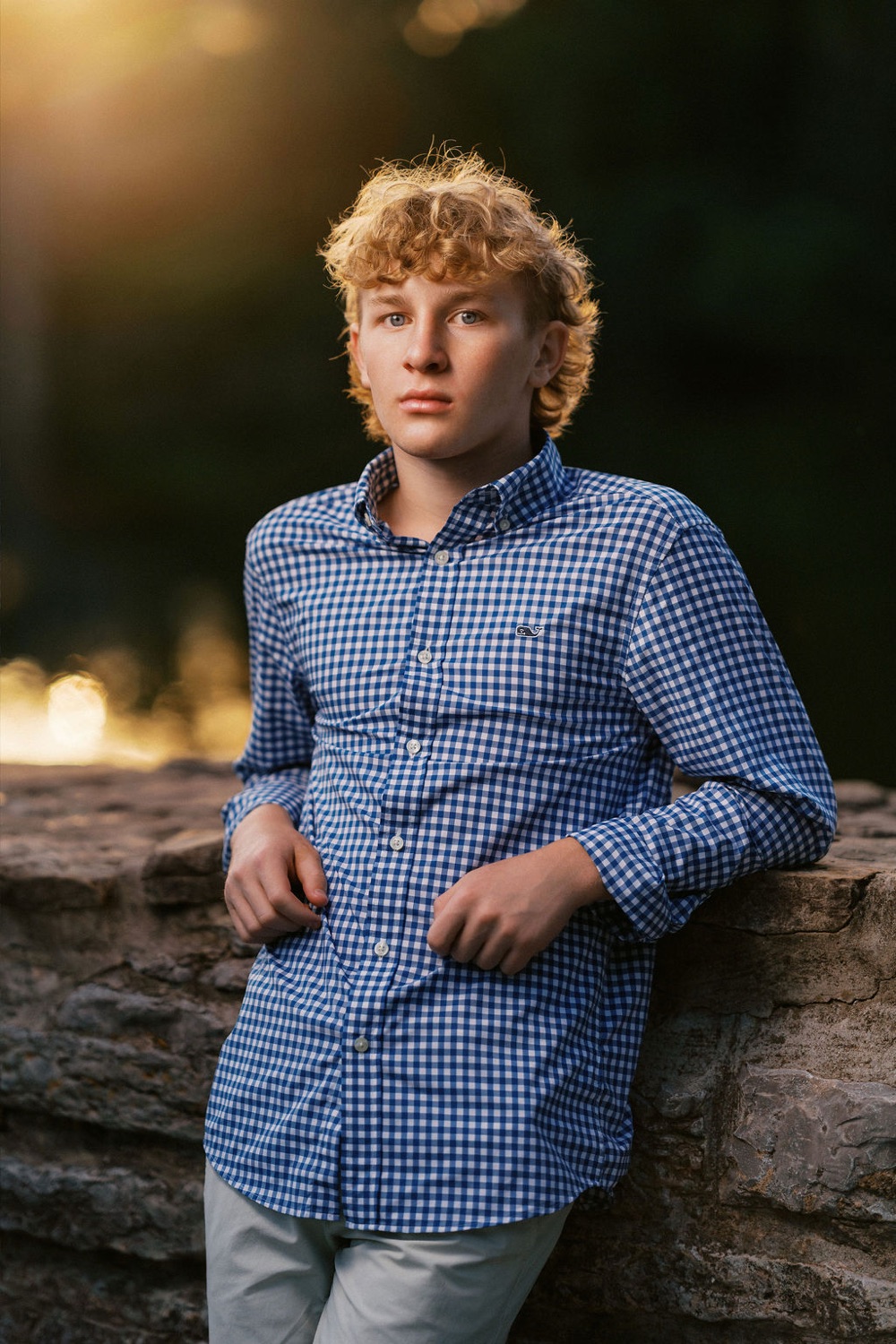 Senior with curly hair against a golden backlit treeline