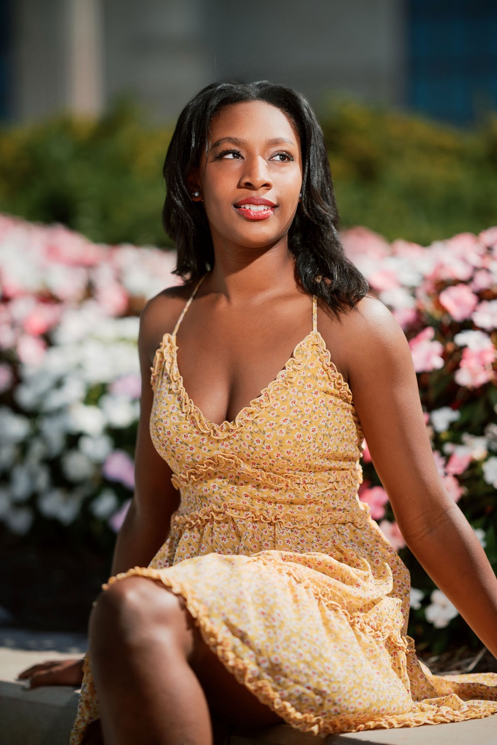 Senior in a yellow dress seated among pink and white flowers