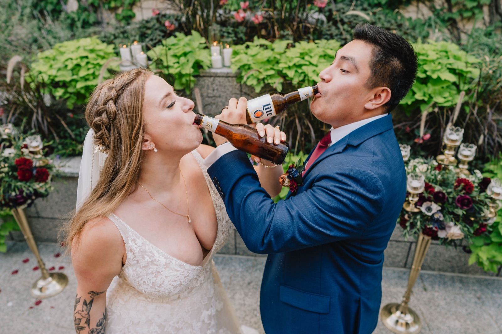 Bride and groom sharing a beer toast in front of florals